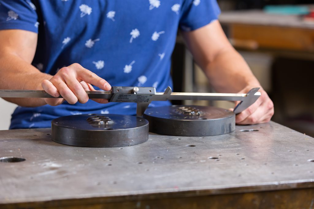 Machinist using calipers to measure steel dies.